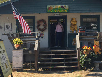 Man entering small building to purchase local honey. Winnie the Pooh bear hanging off porch.