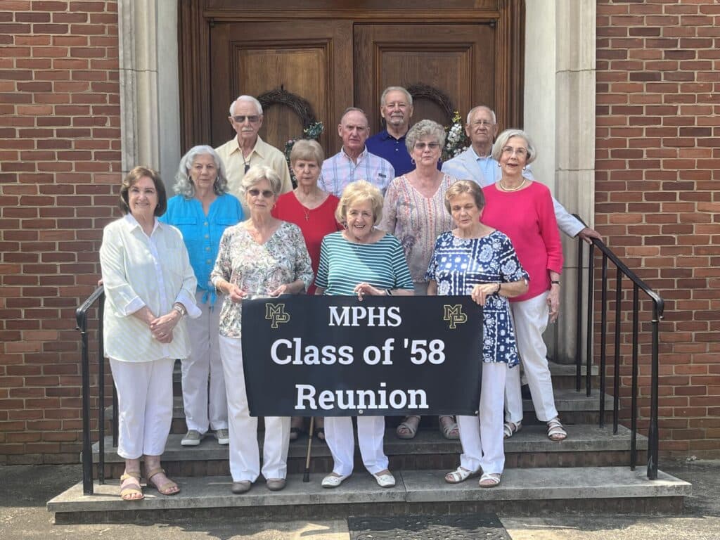 group of seniors standing on steeps in front of high school with sign that reads MPHS Class of '58 Reunion